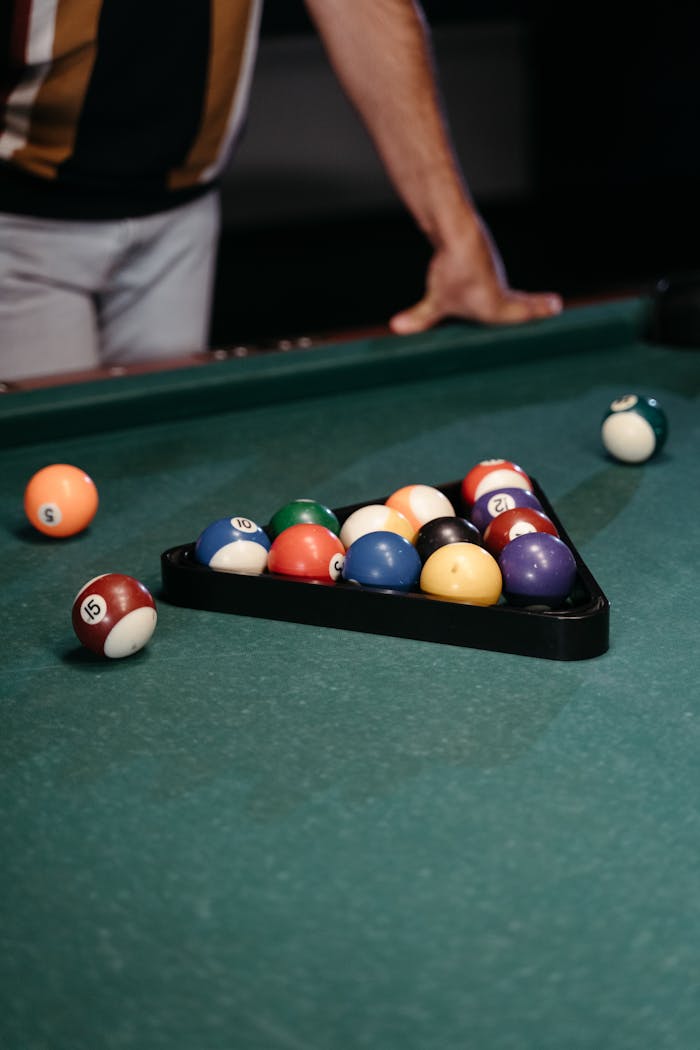 A close-up of a person setting up billiard balls on a pool table, ready for a game.