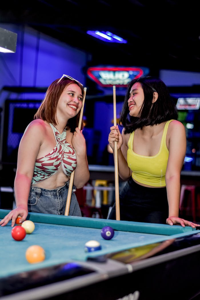 Two women enjoying a fun game of pool in a lively billiard room atmosphere.