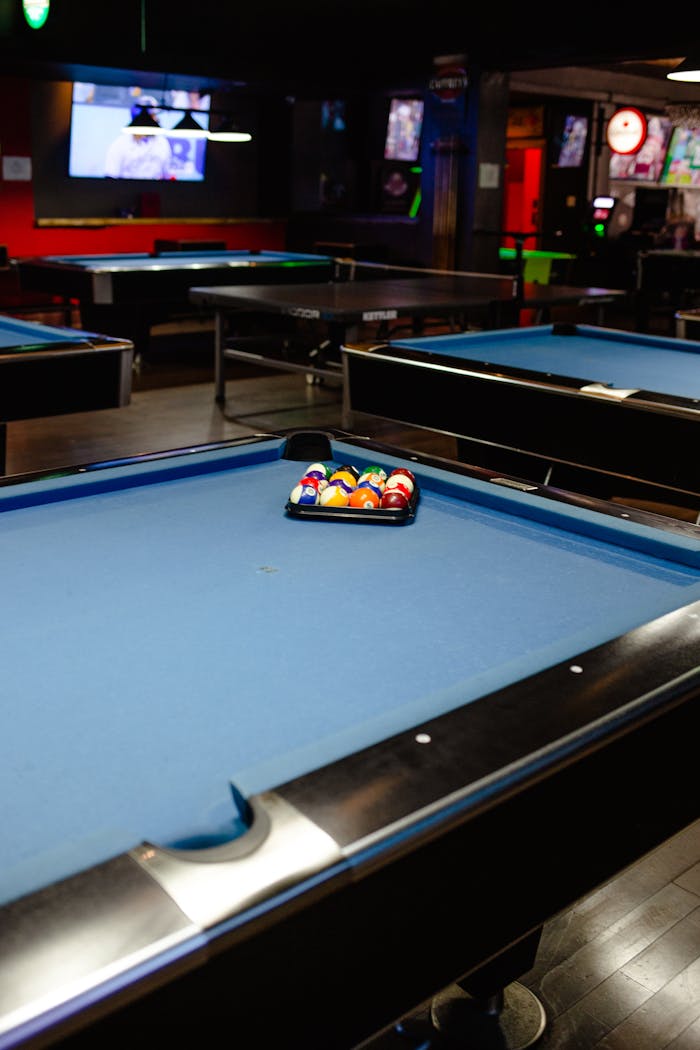 A pool hall setting with a billiard table featuring neatly arranged balls and vibrant interior lighting.