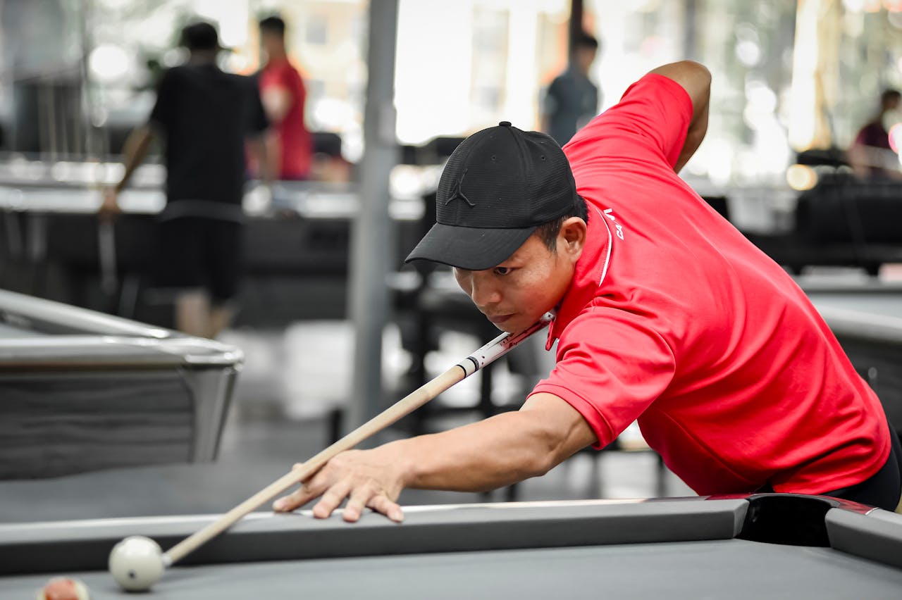 Man in red shirt aiming during a billiards game in a Hà Nội pool hall, Vietnam.
